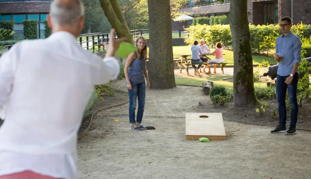 People playing cornhole outdoors with wooden board and bean bags.